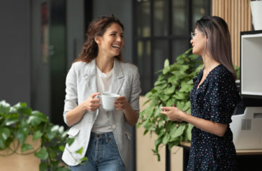 Happy female colleagues talking laughing during break in work space