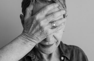 Black and white closeup of older woman with hand covering face