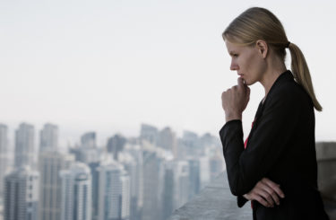 Executive woman thinking at work while looking at the city view from a high-rise. Business career challenges.