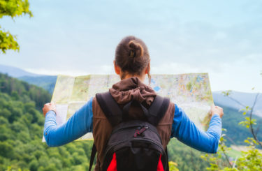 Woman traveler with backpack checks map to find directions in wilderness area, real explorer. Travel Concept