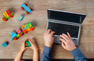 Close up of kids hands playing with colorful blocks near father working on the laptop