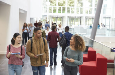 Students holding tablets and phone talk in university lobby