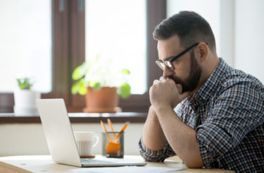 Millennial casual businessman thinking and looking at laptop in office