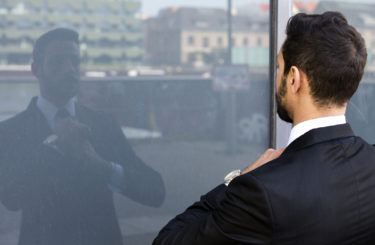 businessman standing outside and looking at his reflection in window