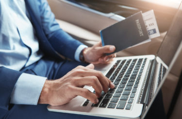 Check in. Cropped image of young businessman in formal wear working on laptop and holding passport with flight tickets while sitting in car. Travel concept. Business concept. Digital technologies