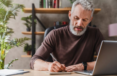 Middle aged businessman in casual clothes making notes in notepad while sitting in his office