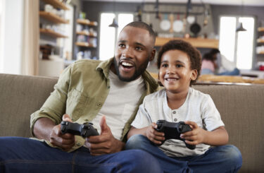 Father And Son Sitting On Sofa In Lounge Playing Video Game