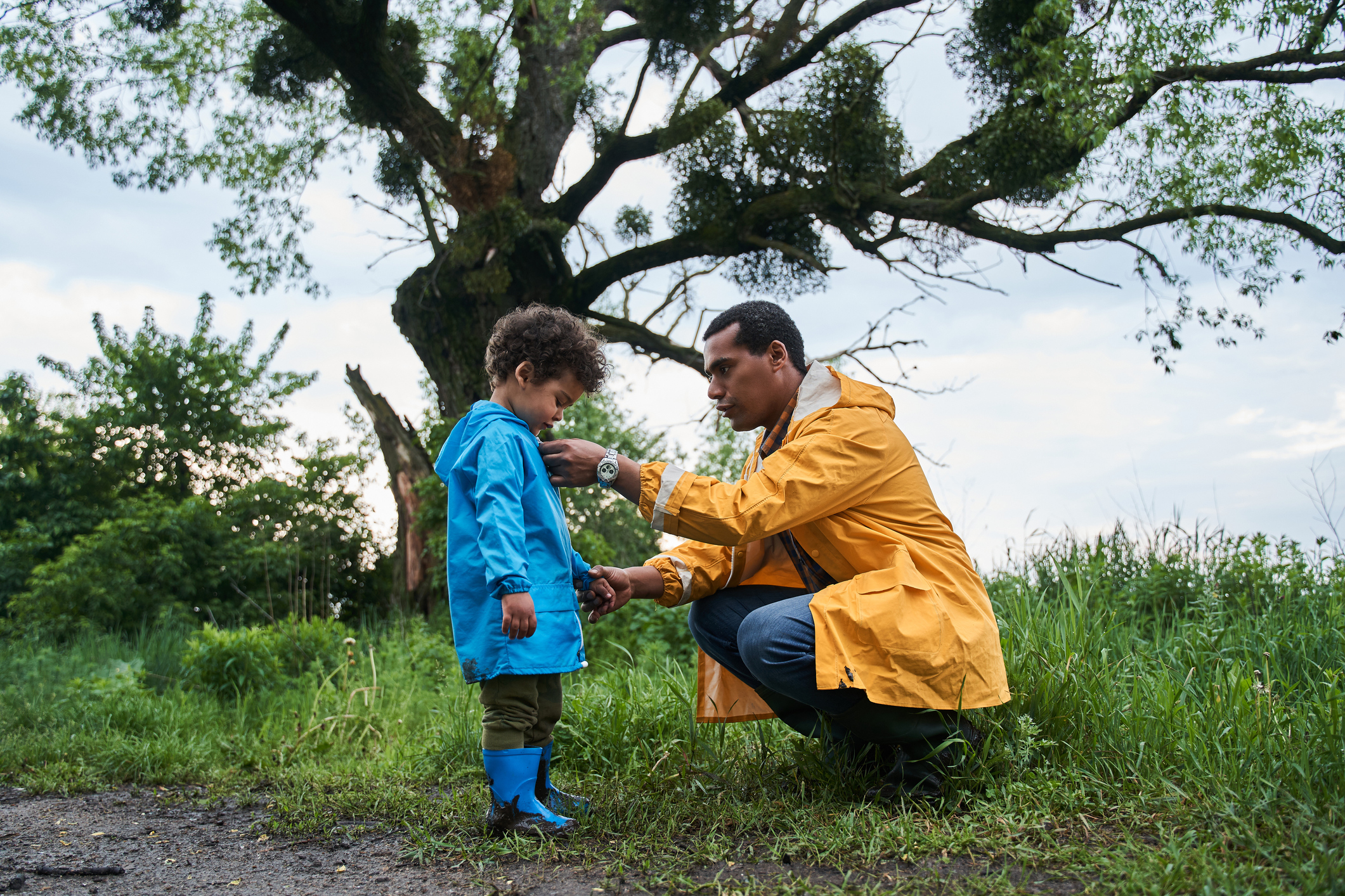 Father helps child to put on raincoat for child