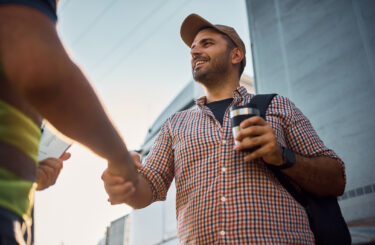 Low angle view of happy truck driver and freight transportation manager greeting on parking lot.