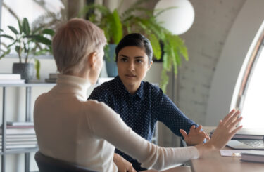 Indian and caucasian businesswomen negotiating sit at desk in office. Lawyer consulting client during formal meeting. Job interview and hiring process. Diverse colleagues discussing project concept