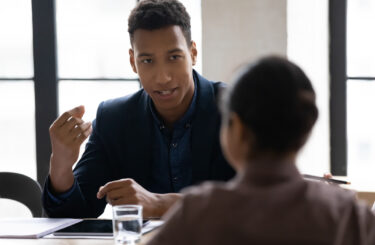 Head shot young african american male manager sharing project ideas with attentive indian colleague at brainstorming meeting, diverse millennial coworkers discussing working issues in office.