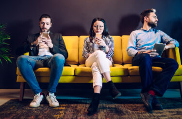 Diverse business people sitting on couch and not talking to each other while using gadgets and checking news and email