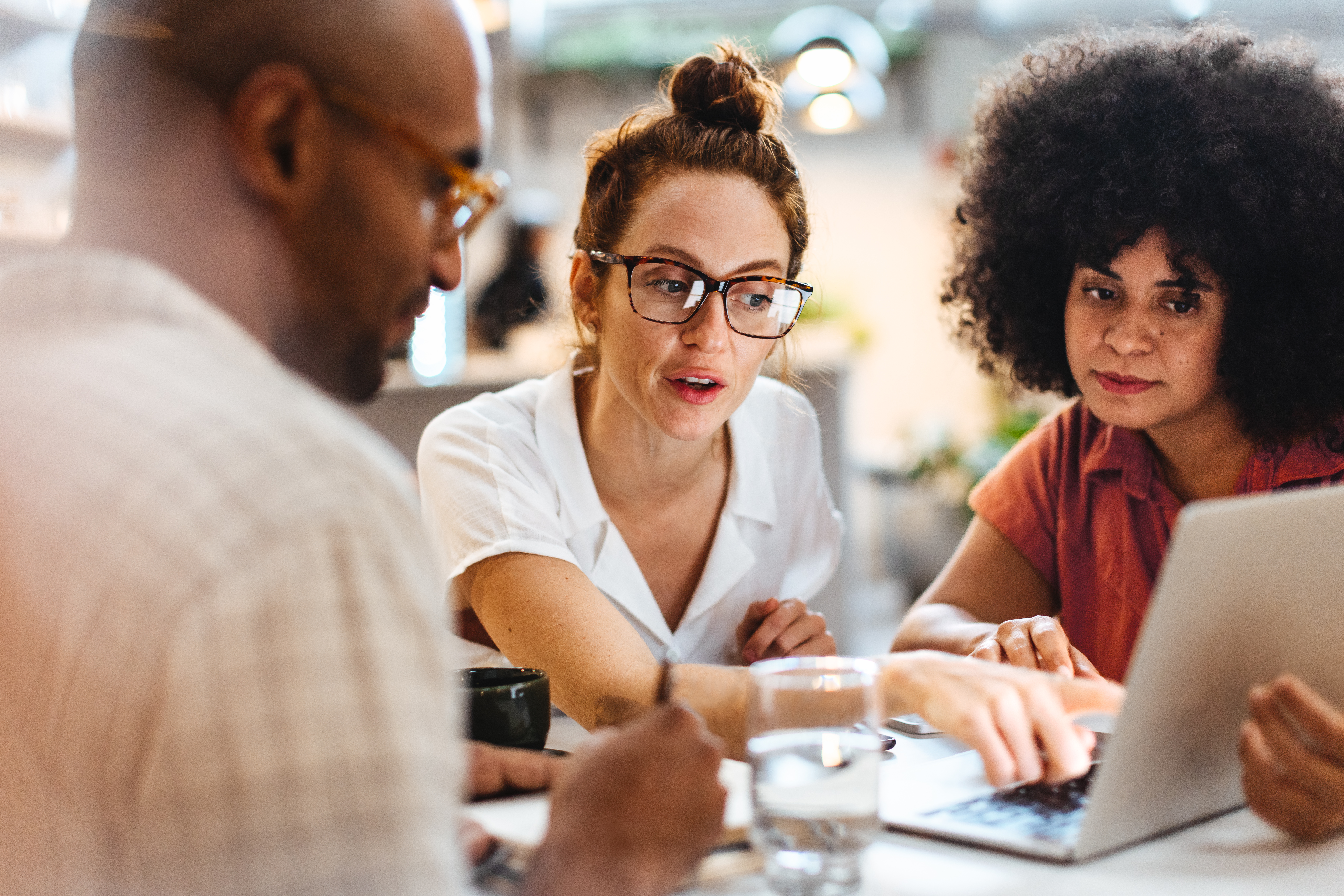 Business women having a work lunch in a café, exchanging ideas and discussing their projects with a client. Young business team using a laptop as they sit around a coffee table.