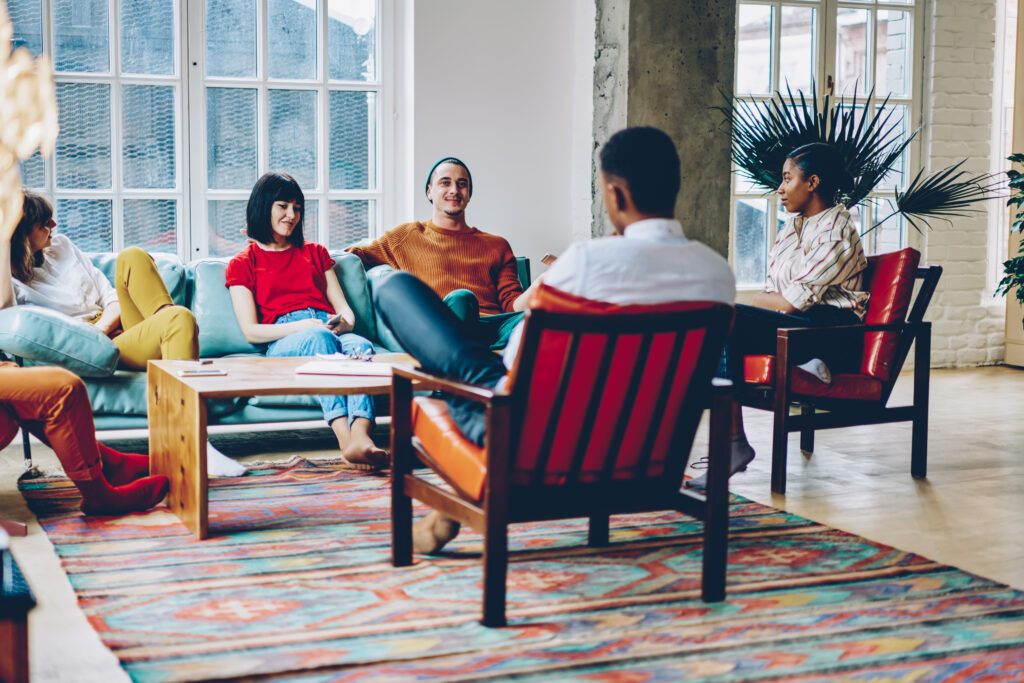 Group of multiracial people resting on comfortable seats around table and communicating with each other in spacious living room at home